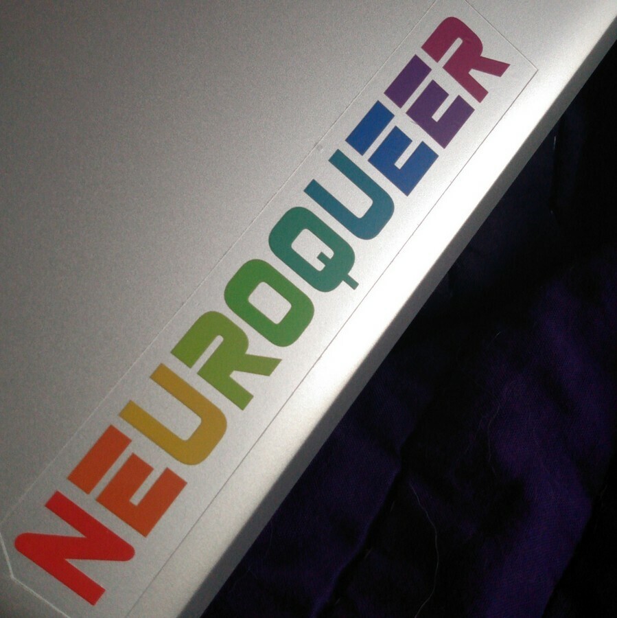 rainbow letters on clear vinyl "Neuroqueer" sticker on a laptop. Five and a quarter inches long by one inch high.