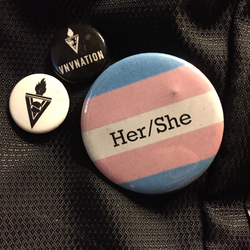 backpack with 2 VNV Nation button and a “her/she” in trans flag colors