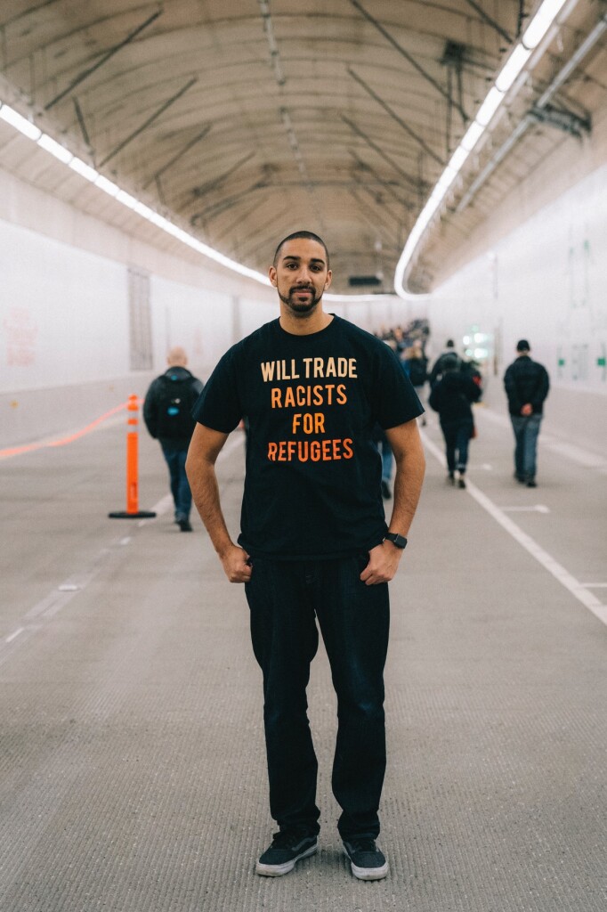 Image of a man in the State Route 99 tunnel in Seattle, Washington with a shirt that reads “Will trade racists for refugees”