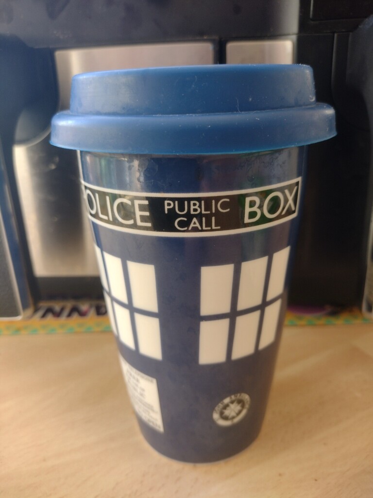 A ceramic reusable coffee cup bearing a police box design, with a blue rubber lid.