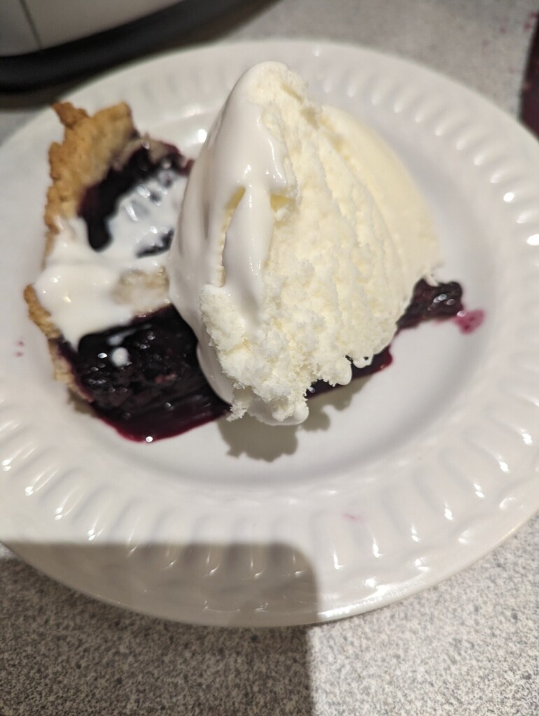 A slice of wild berry pie with a scoop of Coaticook vanilla ice cream on top, on a white plate