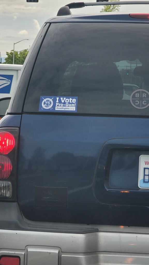 photo of the back of a blue suv with a bumper sticker that says "I vote pro-gun!" 