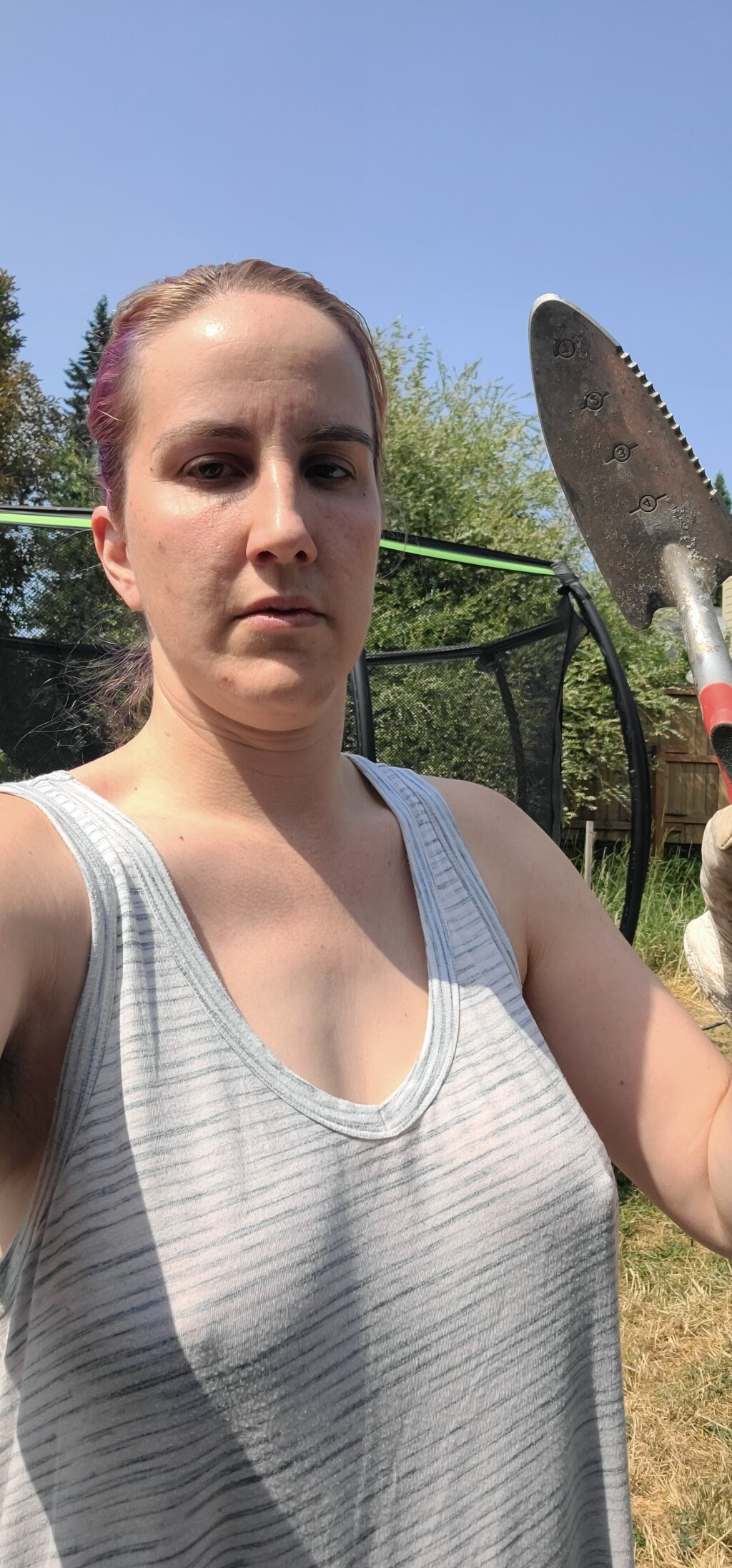 photo of me in our backyard holding up a hand trowel, looking miserable in the heat