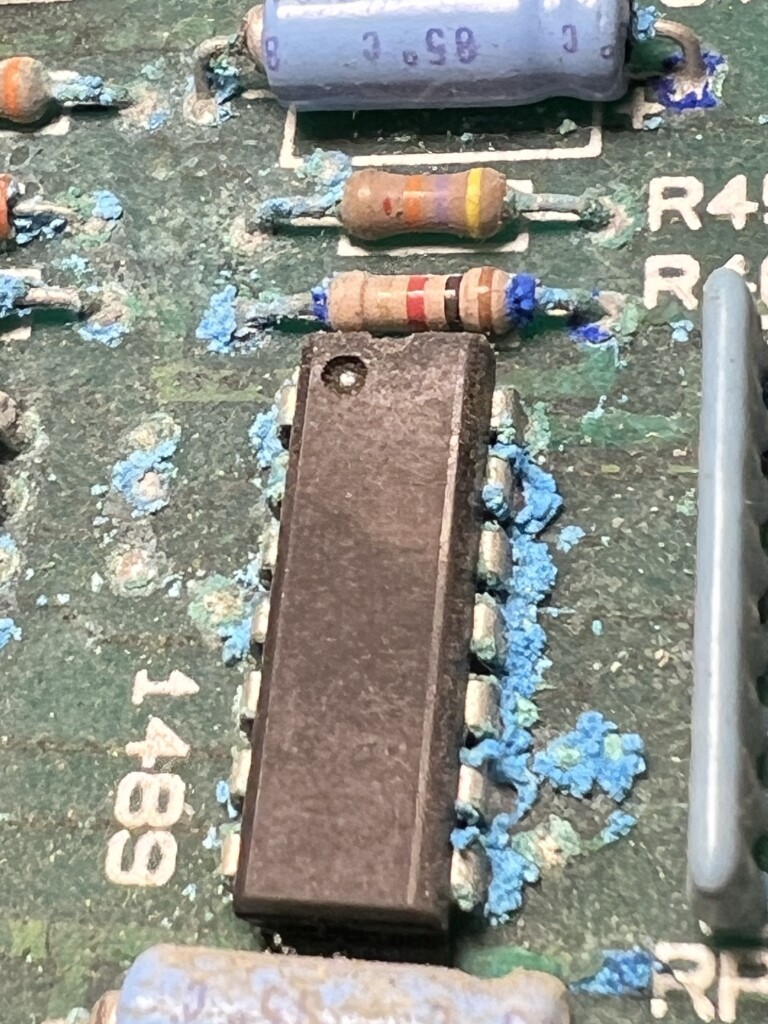 Electronic components on a printed circuit board (PCB), including resistors and an integrated circuit, with signs of corrosion or residue.