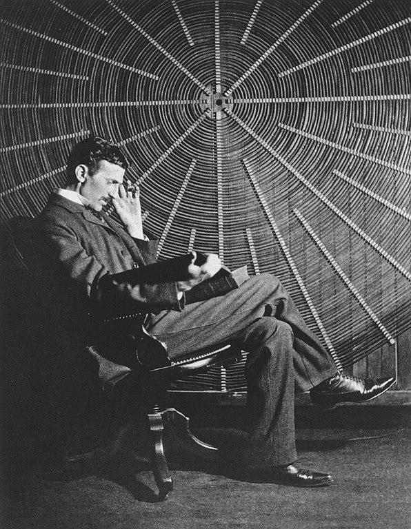 Nikola Tesla, with Rudjer Boscovich's book "Theoria Philosophiae Naturalis", in front of the spiral coil of his high-voltage Tesla coil transformer at his East Houston St., New York, laboratory.

Tesla is typically shown standing confidently, either holding the book or with it placed on a nearby table, symbolizing the connection between theoretical knowledge and practical application. He is dressed formally, reflecting his professional demeanor and the serious nature of his work.