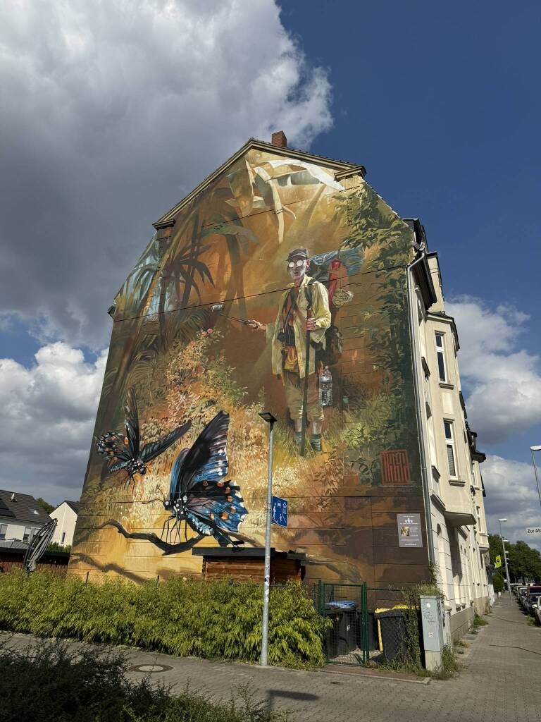 Ein Gemälde auf einer Außenfassade eines Hauses. Zu sehen ist eine Neuinterpretation von Spitzwegs Bild Schmetterlingsfänger. Das Haus steht in Gelsenkirchen.