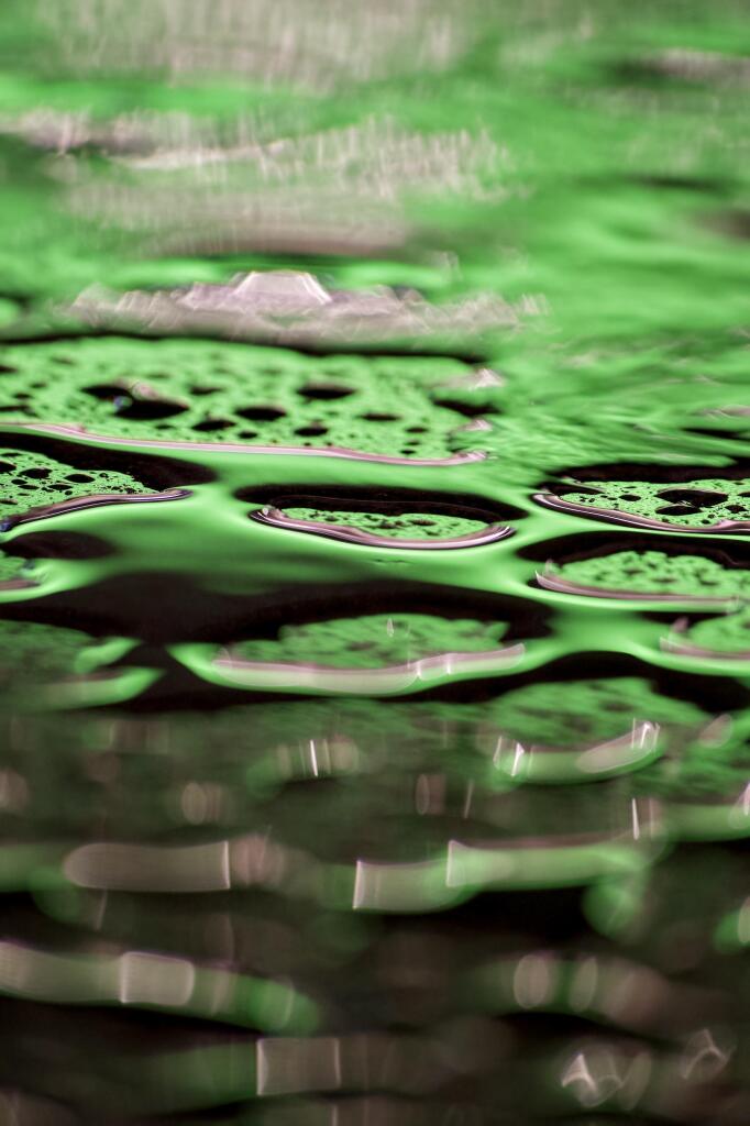 Bright green neon lights reflect in pools of rainwater lying on top of a black marble pillar outside a Glasgow subway station