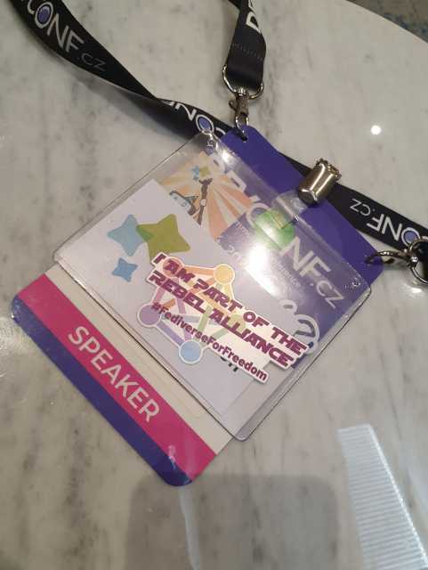Photo oft a Fediverse sticker. In the background the DevConf CZ badge
