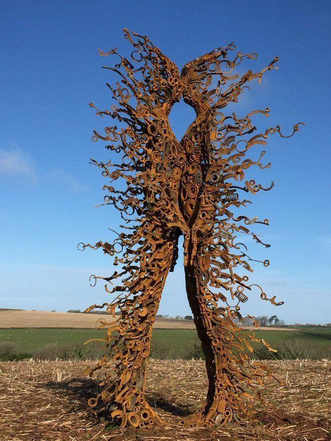 Two women, constructed from scrap metal yet ethereal and windblown kiss in a field