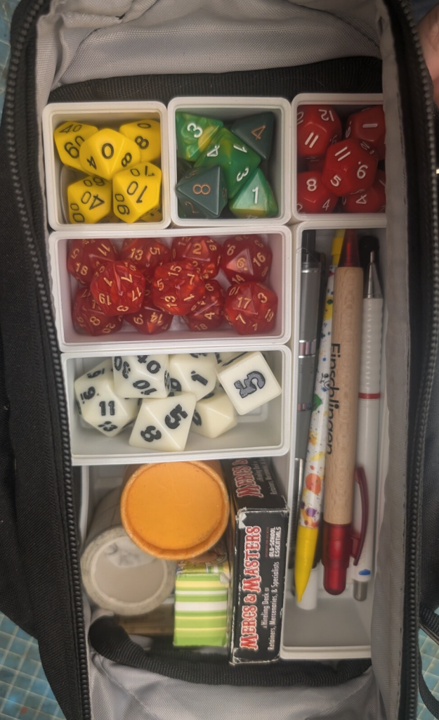 The notepad is gone, now one can see a bunch of dice and the pens and other things.

Everything is in small square or rectangular stacking bins