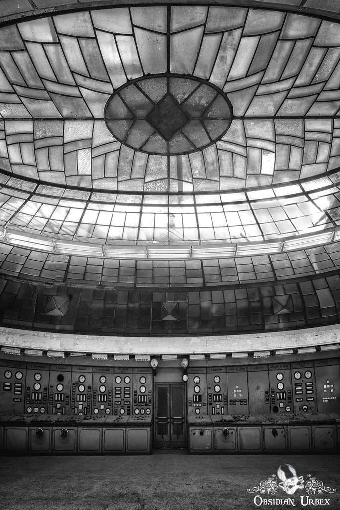 Black and white photo of an abandoned control room with a large domed stained-glass ceiling and old control panels lining the circular walls.