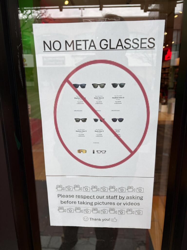 A sign on a store window indicates "NO META GLASSES," featuring images of different sunglasses models. It also includes instructions to respect staff by asking permission before taking pictures or videos, with a friendly "Thank you!" at the bottom.