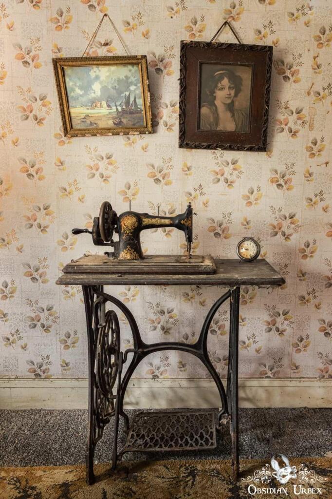A vintage Jones sewing machine on a table against floral wallpaper, beneath two framed pictures.