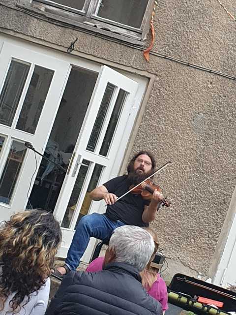 Ein Mann sitzt im Innenhof vom Haus des Wandels und spielt Violine