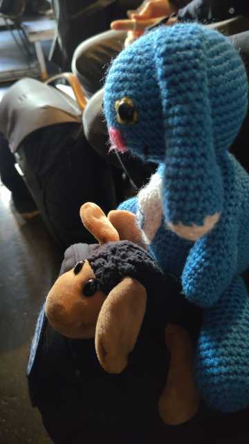 Ein schwarzes Plüschschaf und ein blauer Alien in Hasenform, die auf einem schwarzen Rucksack sitzen.