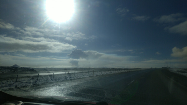 A mushroom cloud over volcanic eruption site seen from afar, through a car's windshield.