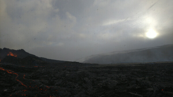 Blizzard over a lava field and an actively erupting volcano.