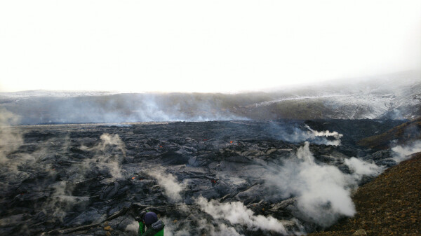 Large, steaming lava field with hills surrounding it.