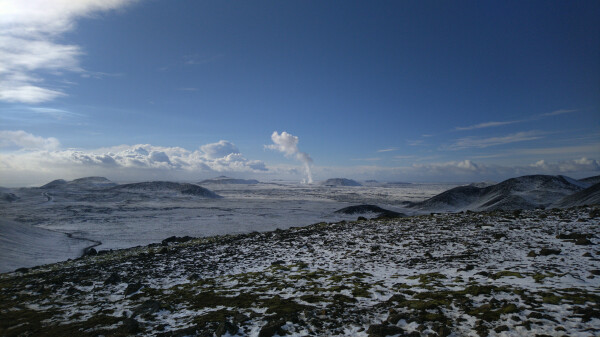 Small, thin mushroom cloud on the horizon. Photo taken from atop a hill, looking down on the flat area with the trail somewhat visible.