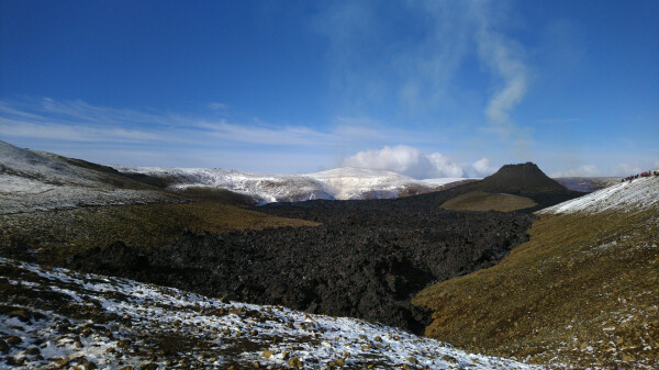 Black solidified lava field, a couple of hundred meters form the volcano cone, between snowy hills. Snow melted around the lava field, proving how hot it still is, even though it doesn't seem so.