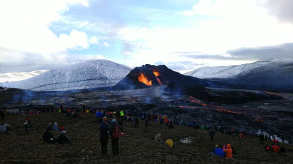 Other side of the volcano, where the cone walls have collapsed. Two simultaneous lava eruptions going, with a lava flow well visible on the lava field.  Hills in the background, people around, marveling at the sight.