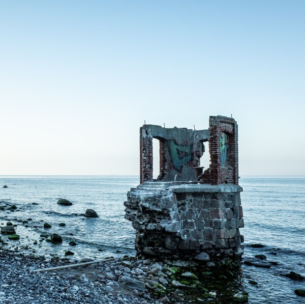 Photograph of a ruin of an old lighthouse on a stone beach with graffiti on it