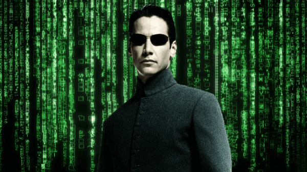 Image of Neo from "The Matrix" wearing a smart black suit and dark glasses, behind him is a green computer screen with lots of letters and numbers