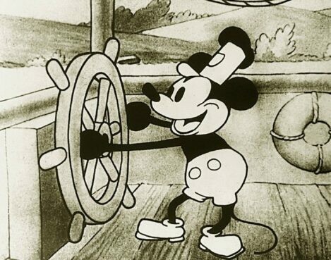 Still from the movie Steamboat Willie. Mickey Mouse is at the wheel of a steamboat, with hills passing in the background.