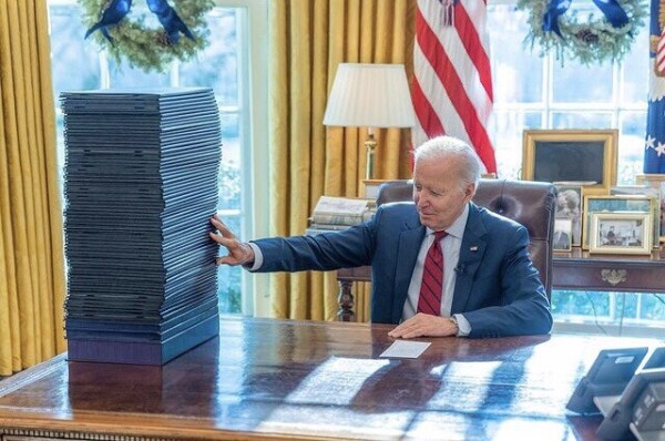 President Biden, sitting at his Resolute desk, looking at the 65 pieces of legislation he signed into law this week. 