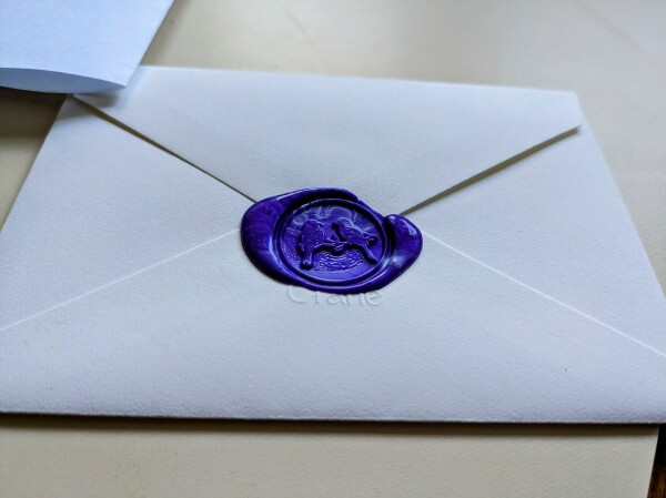 An envelope sealed with purple sealing wax, using a stamp in the shape of two songbirds perched together on a branch