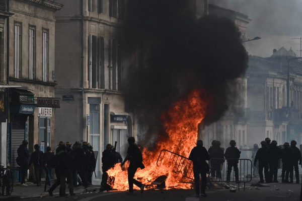 Police stand around a burning barricade in Bordeaux, France during protests over Macron's pension reform in March 2023.