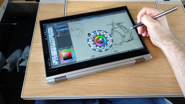 A photography, my pov while i seat in the train with the foldable table in front of my seat, and on it a Lenovo Yoga running Gnu/Linux Fedora KDE Krita, my hand is visible, an i digital sketch on the device with a stylus.