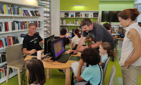 A photo of a part of the library where tables had computers with tablet to do digital painting using Krita. I'm helping a young girl on the photo. She is painting a sunset.