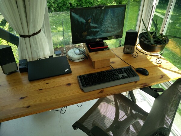 A wooden computer desk overlooking a garden and greenery on a sunny day