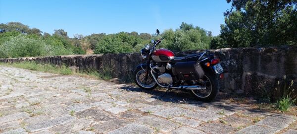 Moto cinzenta e encarnada, clássica, no tabuleiro duma ponte romana.