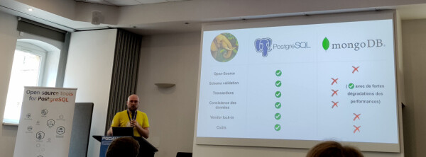 Conférencier en teeshirt jaune, devant une slide qui compare des fonctionnalités entre Postgresql et MongoDb