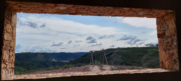 Vista para um baloiço panorâmico com moldura da janela. Só fundo o céu e montes cobertos de vegetação.