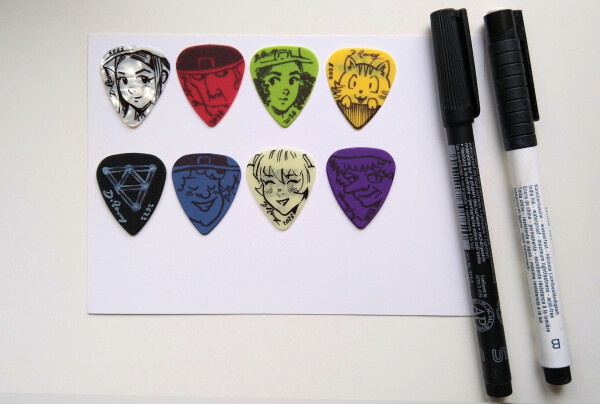 A photo of two pen (white and black) with 8 guitar picks colored. They have drawings of Pepper, Cayenne, Coriander, Carrot, etc...