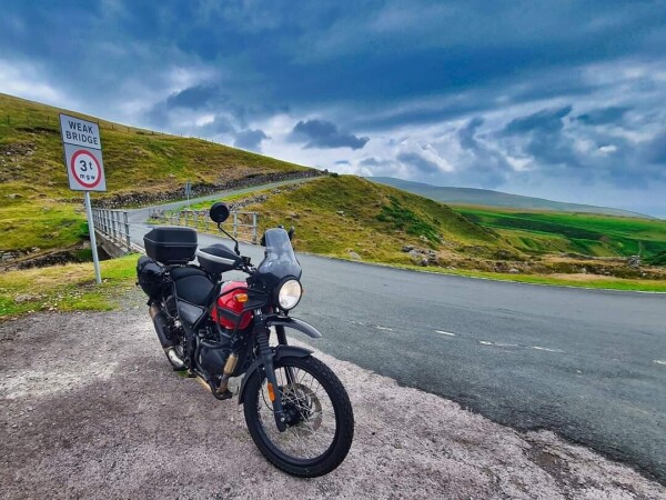 Red Himalayan motorbike at the side of road with hills and a bridge behind