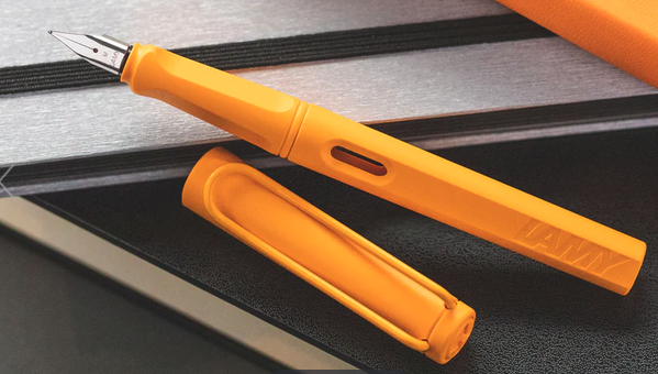 A bright orange fountain pen is shown with the cap removed, and laying diagonally.  It has a matte finish and the orange colour is similar to a ripe mango.