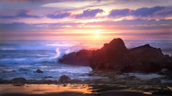 Rocky coast of Sagres, Portugal. Setting sun lights up the churning waves along the rocky coast. Orange sunset with clouds that curl just like the waves.