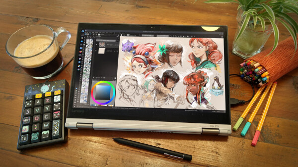 A top down view photo on a wood table, with on it a Lenovo Yoga 370 laptop in tablet mode and with a stylus. The operating system is Fedora Linux, and Krita is running with sketches of random characters on the canvas. Colorful and sketchy. Around the computer: an unusual numeric keypad painted and colorful, a cup of coffee, a plant and felt pen (decorative, to give the photo a bit of color). 

License: Creative Commons Attribution 4.0