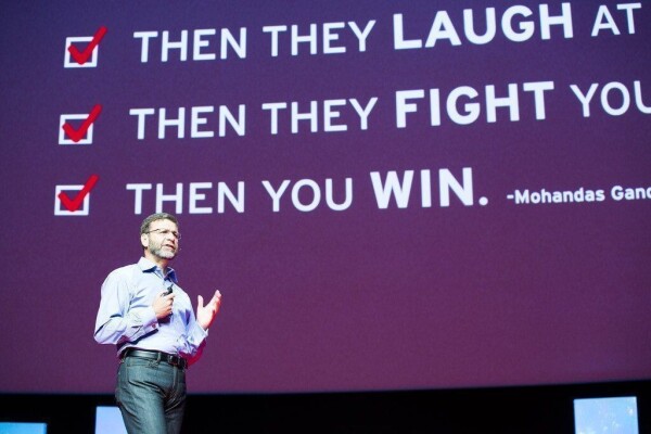 A photograph of Red Hat chairperson Paul Cormier presenting to an audience. In the background, a presentation slide with the misattributed quote bullet pointed.