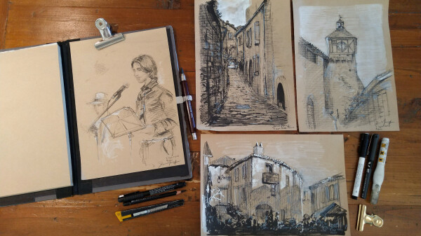 A photo of a table (top view) with four sheets of kraft paper with black and white sketches:
1. A man with long hair, black shirt and a microphone, in background another man in white with a hat.  
2. A street of the village of Penne.
3. The bell tower of the church of Penne.
4. Houses of the village of Penne.