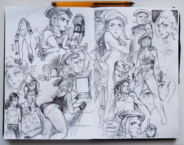 Another (last) photo of my sketchbook, a double page with ballpen sketches, many things are going on: again, Cammy studies. An unfortunate view angle where the back of Cammy is proeminent has a label "Oops! bad view angle" near to it, with a cat showing he is sorry. One portrait of her near many studies tell "C'est difficile!" French for "It's difficult!". A little note writes "maybe more anime" near a portrait with larger eyes and pointy shapes. "Oops too long" near leg in perspective a bit too long. 