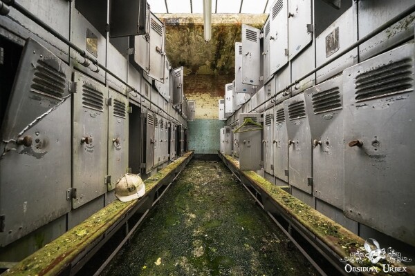 view of lockers, lining both sides. there is a wooden bench in front of each row. a hard hat sits on the left bench