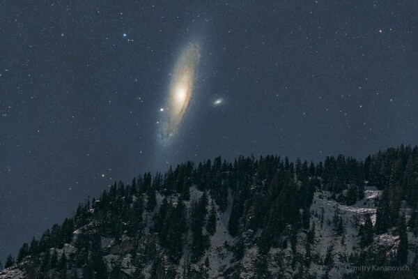 The night sky over a snowy mountain is shown, with the dark sky dominated by a large spiral galaxy -- the Andromeda galaxy.