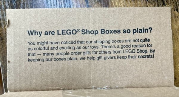 A cardboard box flap reads “Why are LEGO® Shop Boxes so plain?
You might have noticed that our shipping boxes are not quite as colorful and exciting as our toys. There's a good reason for that - many people order gifts for others from LEGO Shop. By keeping our boxes plain, we help gift givers keep their secrets!”