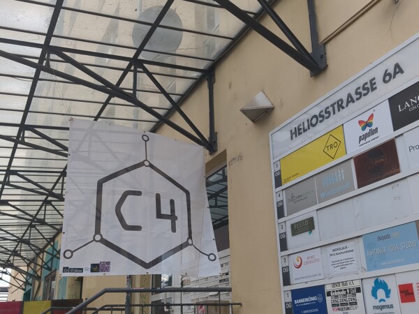 Ein Bild vom Eingangsbereich der Heliosstraße 6a, rechts eine Informationstafel in welcher Etage was zu finden ist, und vor der eingangstür ein c4-Banner mit c4-Logo.