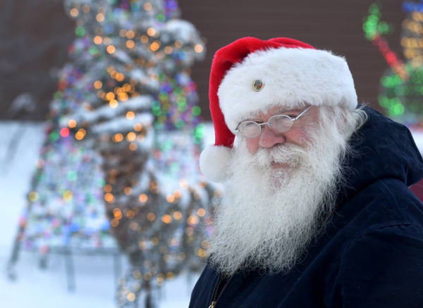 A close-up picture of Santa Claus in North Pole, Alaska. That is his legal name and he has the long white beard, moustache, wire-rimmed glasses, a belly and is wearing a typical Santa hat.